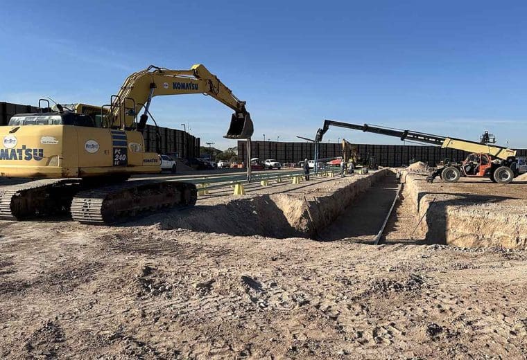Excavator lowering flowline pipe into open trench on a 17-well pad