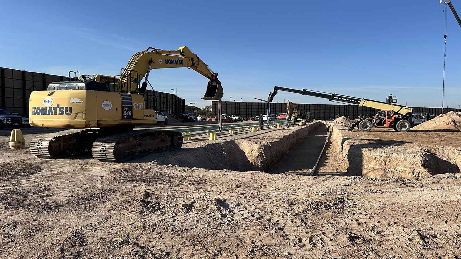 Excavator lowering flowline pipe into open trench on a 17-well pad