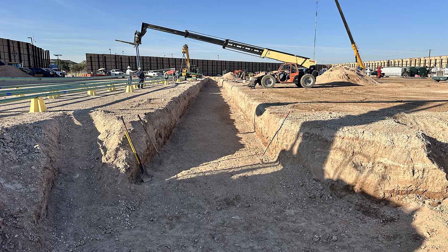 Overview of flowline trench with pipe string laid across a well pad